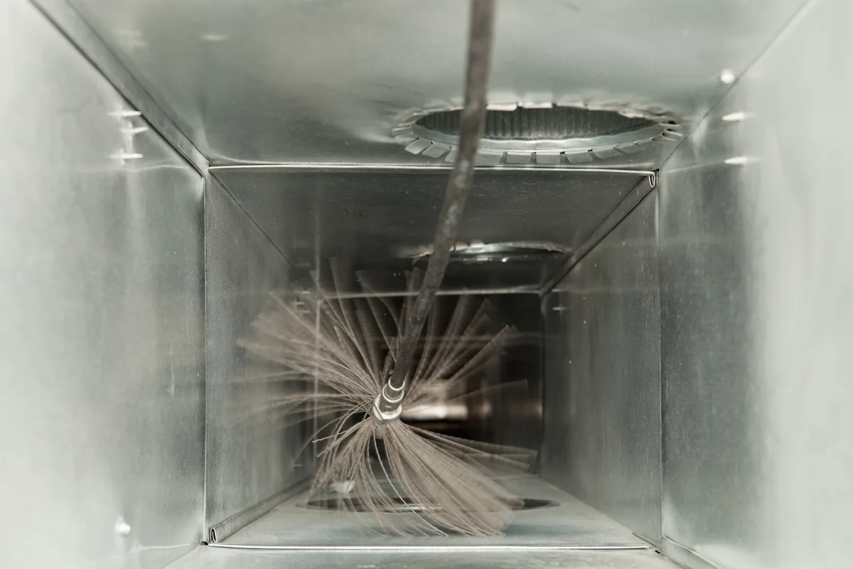 Technician cleaning a residential HVAC duct with a rotary power brush