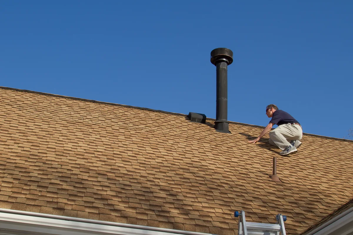 Home inspector on a roof examining a gas vent